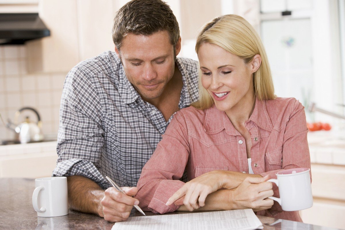 A couple drinking coffee while sitting at a counter and signing a document. 