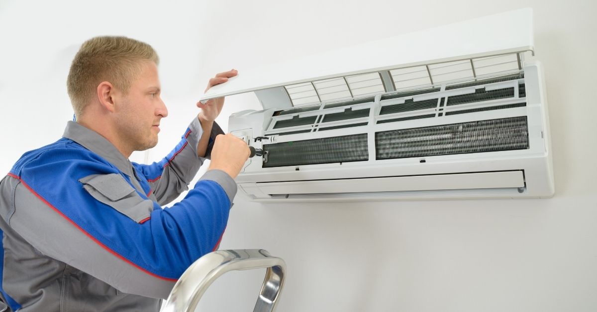 A technician uses a screwdriver to check the mini-duct less unit hanging on a white wall